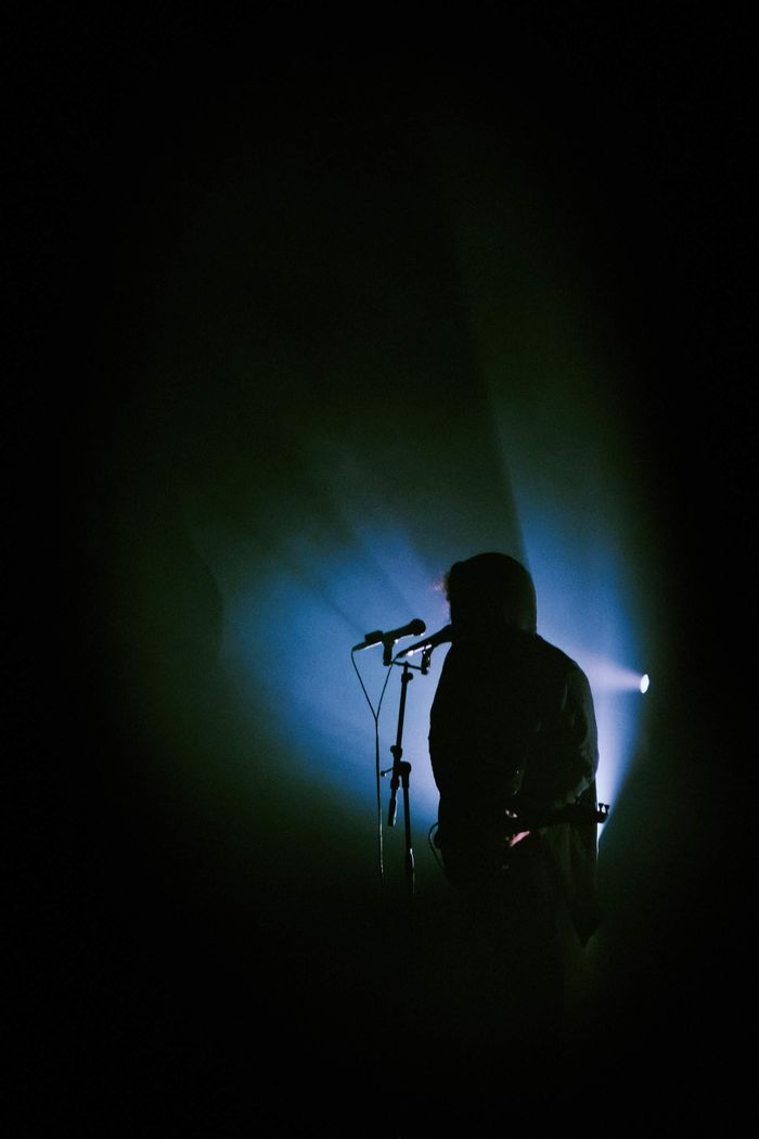services-04 Dramatic silhouette of a musician singing under bright stage lights during a live performance at night.